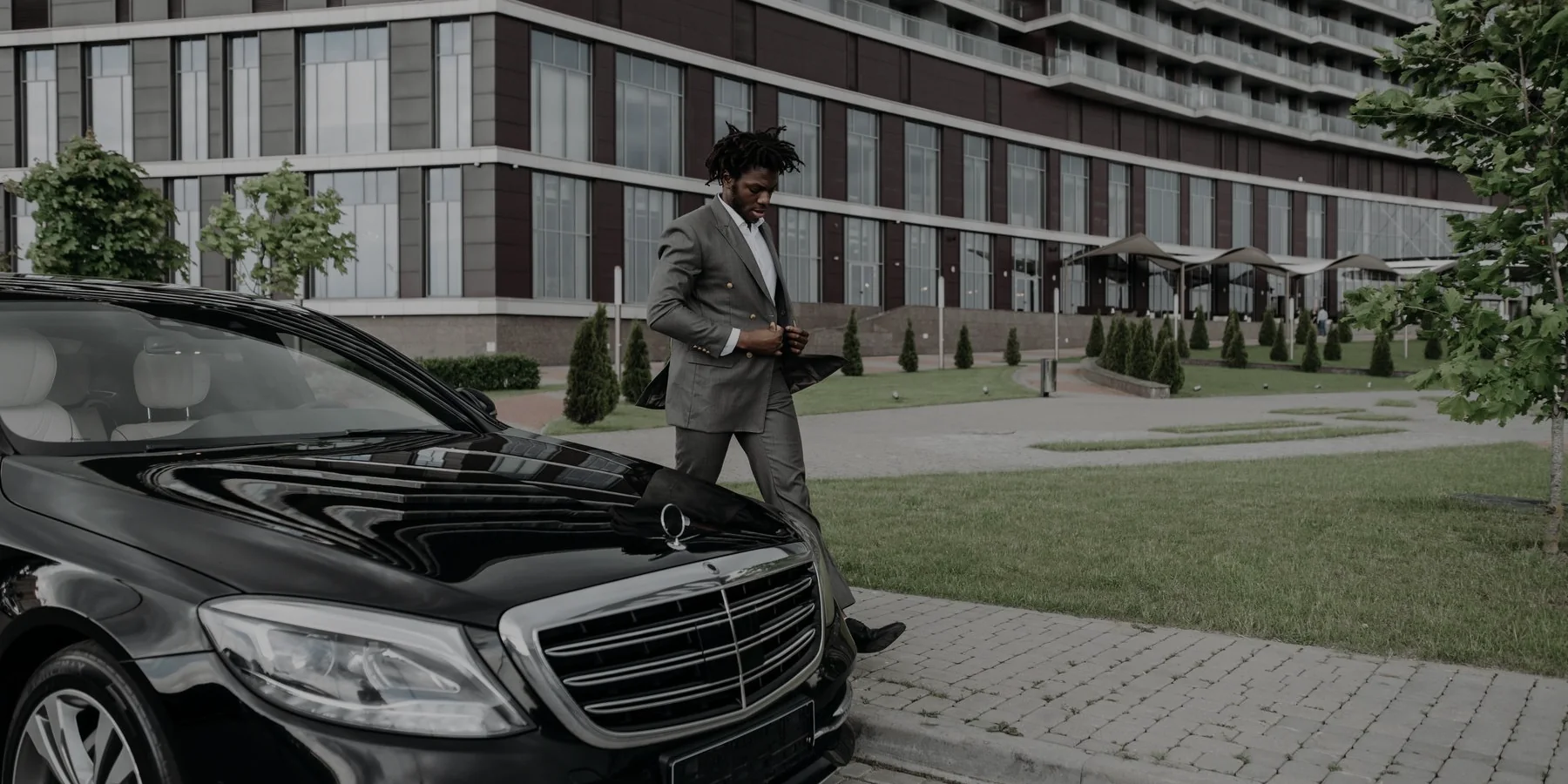 A businessman walking past a black sedan outside an office