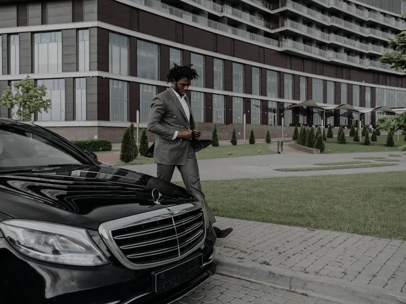 A businessman walking past a black sedan outside an office