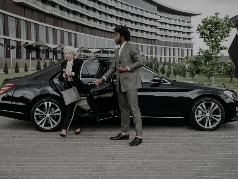 A chauffeur helping a passenger out of a black sedan
